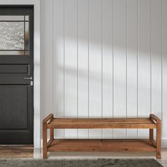 a wooden bench sitting in front of a door next to a rug on the floor