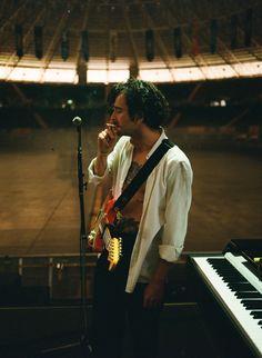 a man singing into a microphone while standing next to a keyboard in front of an empty stadium