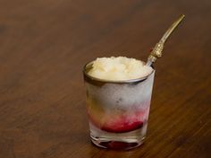 a small glass filled with ice cream sitting on top of a wooden table next to a spoon