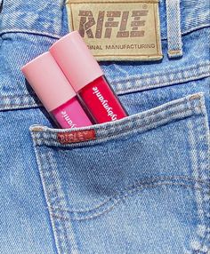 two pink lip glosses sticking out of the back pocket of a pair of jeans