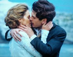 a man and woman kissing each other in front of a blue sky with mountains behind them