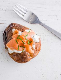 a piece of bread with salmon and cream cheese on it next to a fork, sitting on a white surface