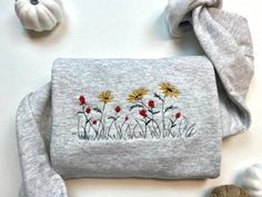 a gray purse with yellow and red flowers embroidered on it next to two white pumpkins