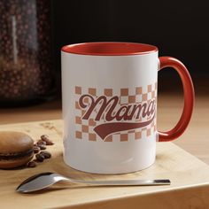 a red and white coffee mug sitting on top of a wooden table next to a spoon