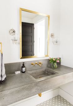 a bathroom sink sitting under a large mirror next to a vase with flowers on it