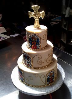 a three tiered cake with an ornate cross on top is sitting on a table