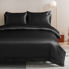 a bed with black sheets and pillows on top of it in a room next to a lamp