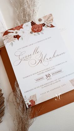 an elegant wedding card with flowers and leaves on the front is displayed next to some dried grass