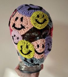 a crocheted hat with smiley faces is held up in front of a white wall