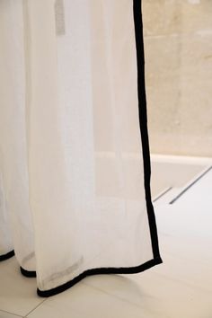 a white curtain with black trim hanging from it's side