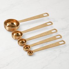 gold measuring spoons and measuring cups lined up on a marble surface