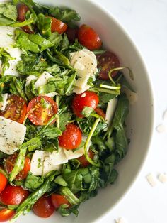 a salad with tomatoes, mozzarella cheese and spinach leaves in a white bowl