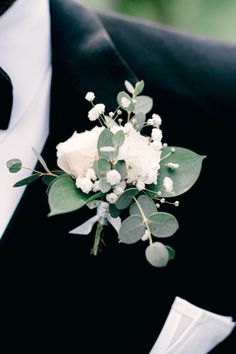 a boutonniere with white flowers and greenery is worn by a man in a tuxedo