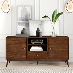 a wooden sideboard with two plants and pictures on the wall in front of it