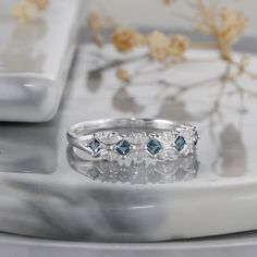 three stone ring sitting on top of a white plate next to flowers and a glass vase