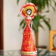 a red and yellow vase with a skeleton decoration on it's head sitting on a glass table