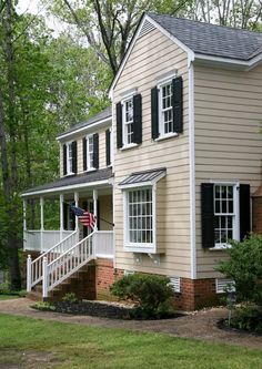 a house with black shutters and white trim on the front door, stairs leading up to the second story