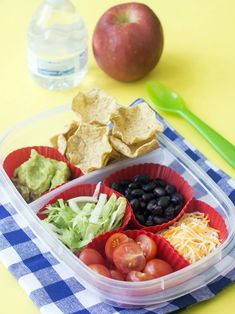 a plastic container filled with different types of food next to an apple and spoons