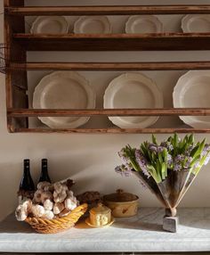 a shelf with plates, flowers and wine bottles on it next to a basket filled with bread