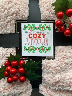 two christmas stockings with holly and red berries on them, next to a sign that says have yourself a cozy little christmas