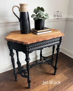 a wooden table with a vase and books on it next to a plant in a pot