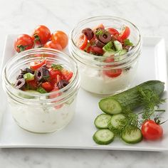 three glass jars filled with cucumbers, tomatoes and olives on a white plate