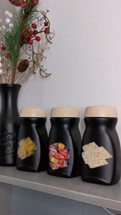 three black vases with different types of food in them sitting on a shelf next to a potted plant