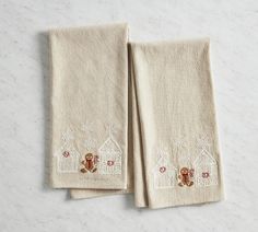 two towels with embroidered houses on them sitting next to each other in front of a marble counter top