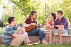 four people sitting on a bench and playing guitar in the park stock - fotor