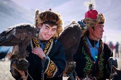 two men in native garb with large birds on their shoulders and one man holding an eagle