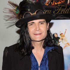 a man with long hair wearing a black hat and blue shirt standing in front of a movie poster