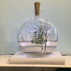 a snow globe with trees in it sitting on top of a white tablecloth covered shelf