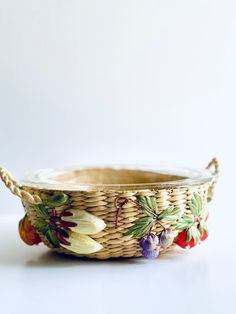 a wicker basket with flowers painted on the side and rope around the rim, sitting on a white surface