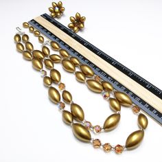 *Description: This is a beautiful mid-century necklace and earring set from the late 1950s. The colors and style are representative of this time period with the large metallic pearled finish oval beads with topaz Austrian Crystals as accent beads. The matching earrings have one crystal in the middle and six of the gold metallic beads around the center in a flower design. The necklace has aurora borealis rhinestone bars near each end. This is a great mid-century set to add to your favorite vintag Glitter Necklace, Crystal Beaded Necklace, Formal Earrings, Necklace Matching, Vintage Christmas Gifts, Crystal Bead Necklace, Oval Beads, Vintage Lucite, Necklace And Earring Set