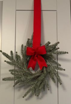 a christmas wreath hanging on a door with a red ribbon around it and evergreen branches