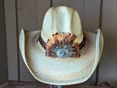 Get ready to rock out at your next country music festival with our Roo Palm Leaf Gus Hat. Made with durable palm leaf and adorned with a feather fan and hat band, this western hat is perfect for cowboys and cowgirls alike. Embrace the Nashville spirit and go country with our stylish and practical hat. There is a wire in the edge of the brim that can be slightly shaped. The brim is 4" and the crown is 5 1/2". Stampede strings are attached which will make it a great hat for those windy days. The feather fan is custom made with a selection of complementing feathers and accented with a Concho. Western Style Concho Hats For Country Events, Southwestern Feather Hat Band For Country Events, Feathered Hat Bands For Beach Events In Summer, Western Hat Bands With Feathers For Rodeo, Western Festival Hat Bands With Feathers, Western Style Feather Hat Bands For Festivals, Western Hat Bands With Feathers For Festivals, Western Summer Hats With Feathers, Feathered Hat Bands For Country Events In Summer