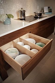 an open drawer in the middle of a kitchen counter with plates and cups on it