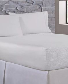 a bed with white sheets and pillows on top of it next to a brick wall