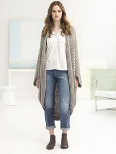 a woman standing in a white room wearing jeans and a cardigan sweater with an open front