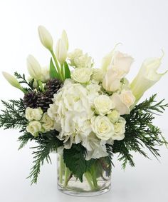 a vase filled with white flowers and greenery on top of a table next to a pine cone