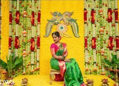 a woman in a green and pink sari sitting on a chair with flowers behind her