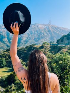 a woman with long hair wearing a black hat and white tank top is looking at the mountains