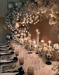 a long table is set with silver and white balloons, candles, and wine glasses