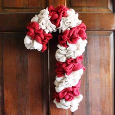 a red and white wreath is hanging on the front door, with fabric flowers around it