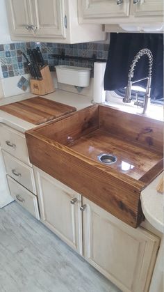 a kitchen sink made out of wood in front of white cabinets and counter tops with utensils on it