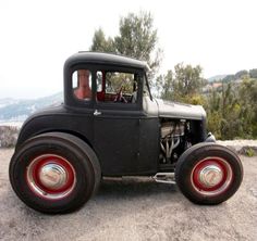 an old black truck with red rims parked on the side of a mountain road