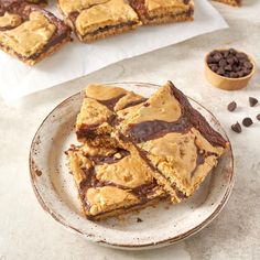 chocolate and peanut butter bars on a plate next to two bowls of chocolate chips, with one cut in half