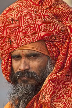 a man with a beard wearing a red turban and orange shawl on top of his head