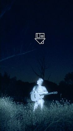 a man holding a guitar in the middle of a field at night with an envelope above him