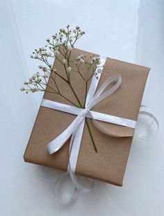 a present wrapped in brown paper with a white ribbon and flower on the top is sitting on a table